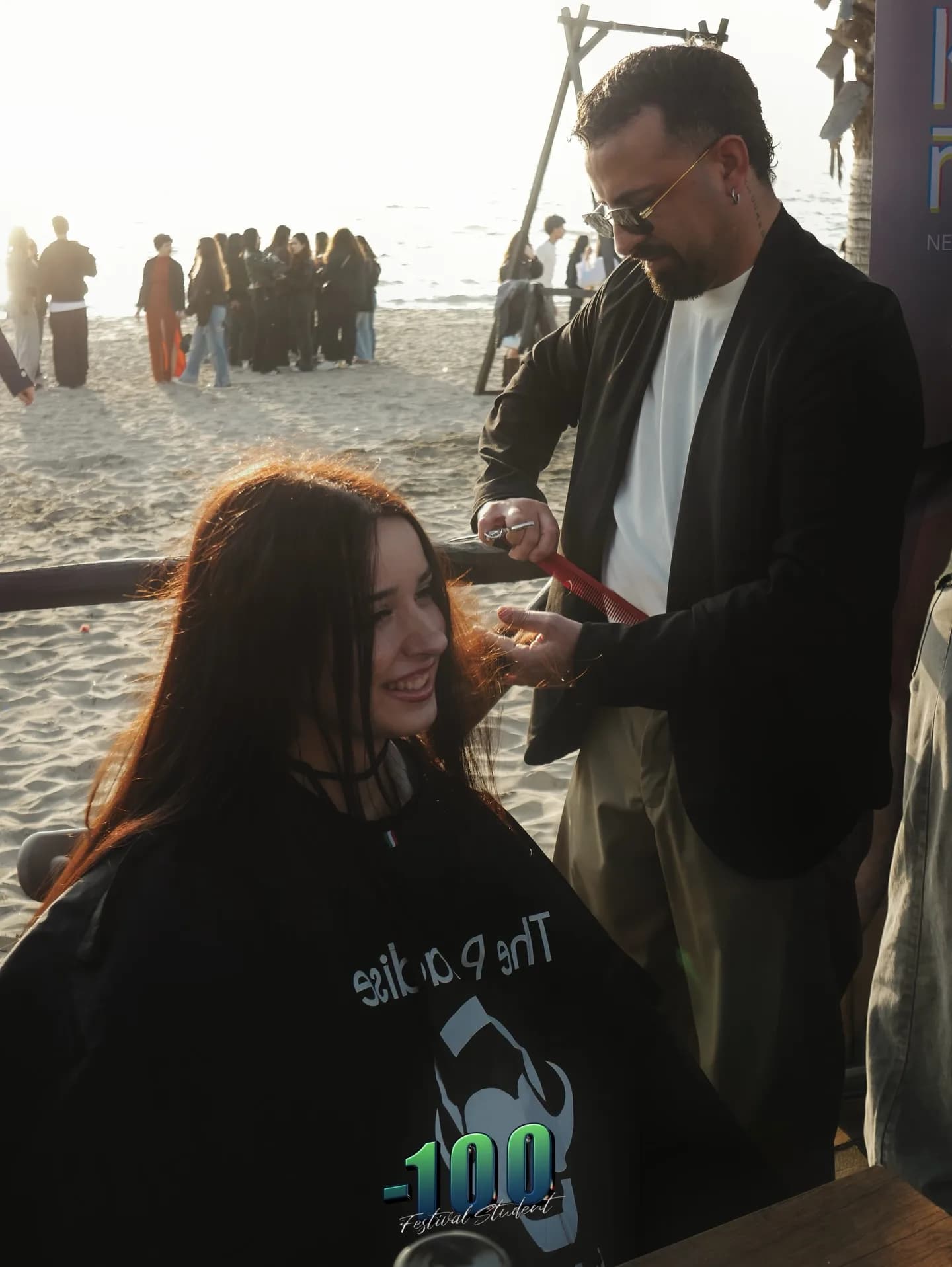 Un barbiere taglia i capelli a una ragazza seduta in spiaggia.